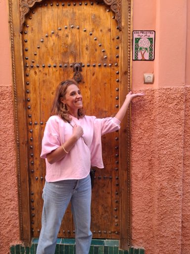 Femme souriante devant une porte en bois ornée d'un motif coloré.
